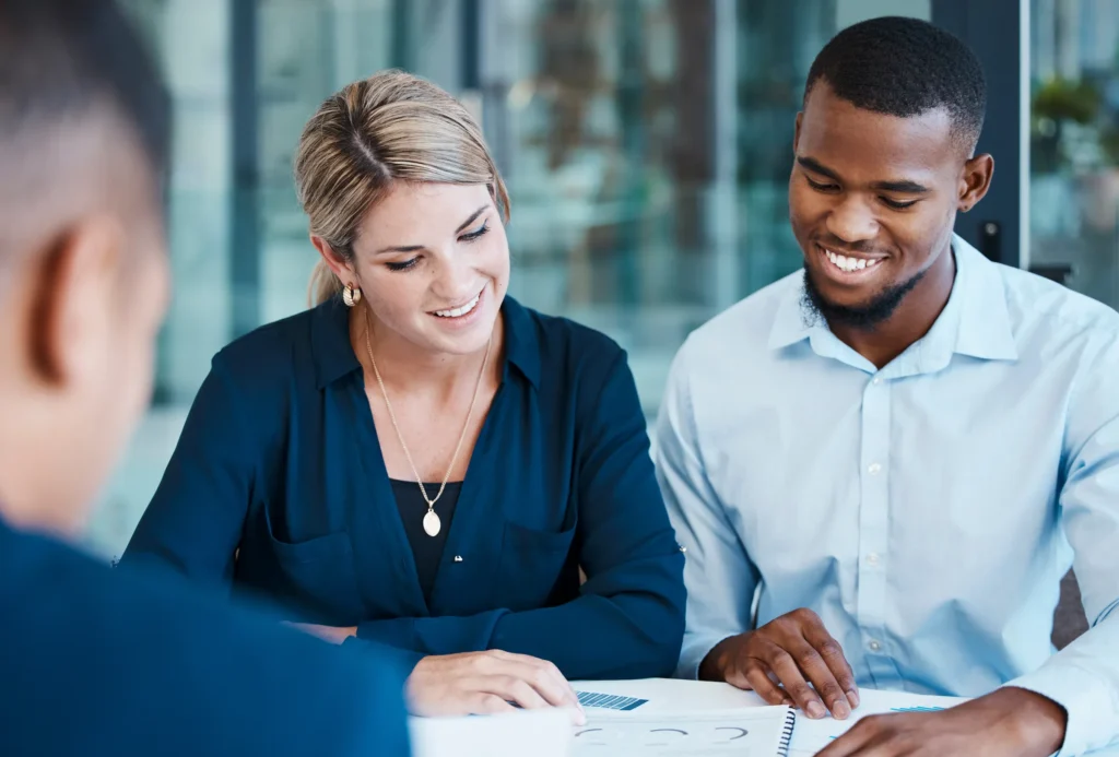 Three colleagues smiling while reviewing paperwork together at a table