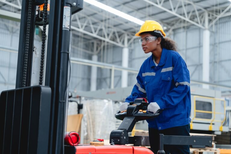 A warehouse employee in a hard hat and work uniform operating equipment on the floor